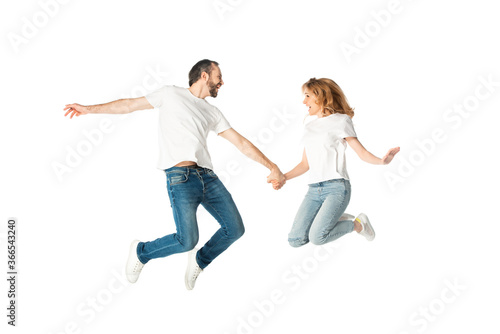 happy adult couple in white t-shirts holding hands while jumping isolated on white