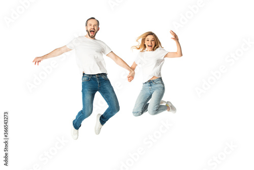 happy adult couple in white t-shirts holding hands while jumping isolated on white