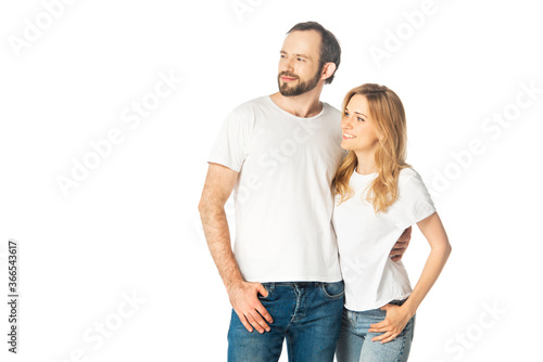 cheerful adult couple in white t-shirts embracing and looking away isolated on white