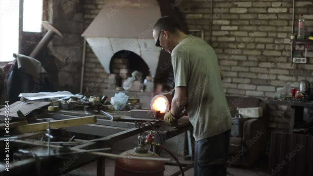 Manipulation with red-hot iron. The blacksmith pulls out an iron bar from the oven and bends it while it is still hot. Side view Manipulation with red-hot iron. The blacksmith pulls out an iron bar from the oven and bends it while it is still hot. Side view