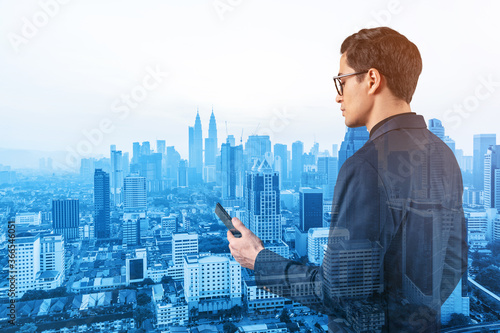 Canvas Print Young handsome businessman in suit and glasses using phone and thinking how to tackle the problem, new career opportunities, MBA