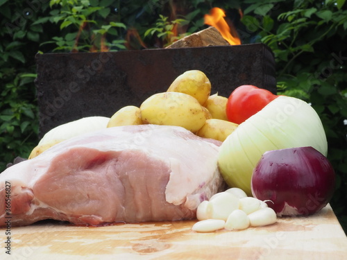 fresh pork loin on the bone on a wooden Board with vegetables. delicious meat with raw potatoes, onions, tomatoes on the background of a burning grill.