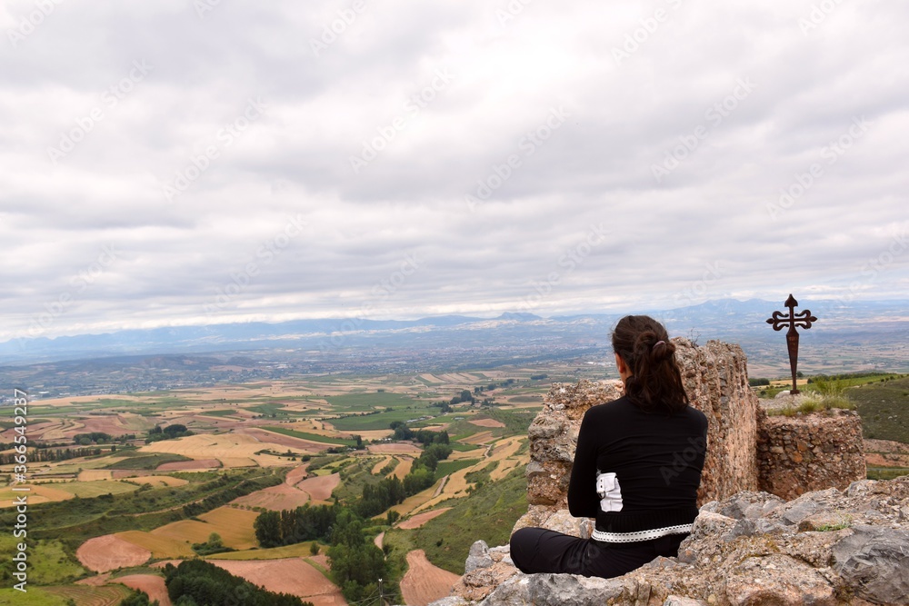 Woman enjoying a moment of inspiration, meditation and fresh air from the top of the Clavijo castle, fields of cultivation in the background.