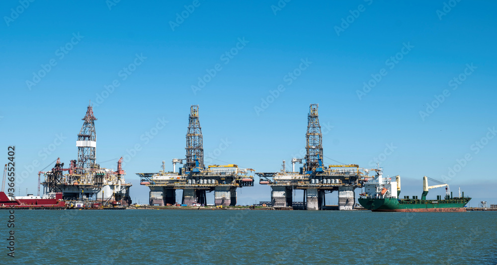 A ship sails by three offshore oil rig platforms in dry dock along the shipping channel at Port Aransas, Texas.