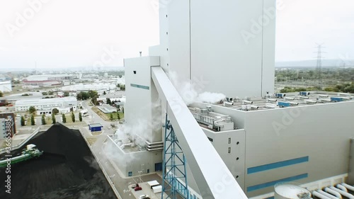 Drone flight towards modern building at a european coal power plant with smoke and grey skies