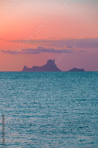 The magic  famous rock of Es Vedra  Ibiza  from the passenger port of Formentera. Ibiza s most popular icon and symbol  said to be magic and mysterious. Soft pink sunset light and blue sea.