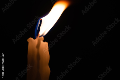 Close-up of a yellow candle shining in a black background.