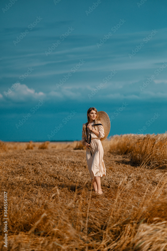 Attractive and beautiful girl in a beige midi dress with a big straw hat, in a wheat field Attractive and beautiful girl in a beige midi dress with a big straw hat, in a wheat field