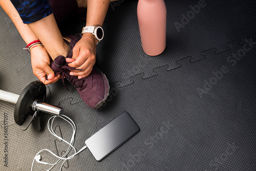 Closeup woman lacing footwear to do exercise at gym with copy space for text. Concept of healthy life and sport. Black rubber floor mat and tiles inside a gym.