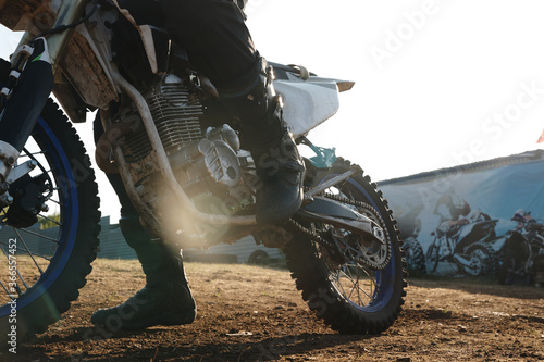 Unrecognizable motorcyclist shifting pedal while preparing for riding motorbike outdoors, sunlight effect