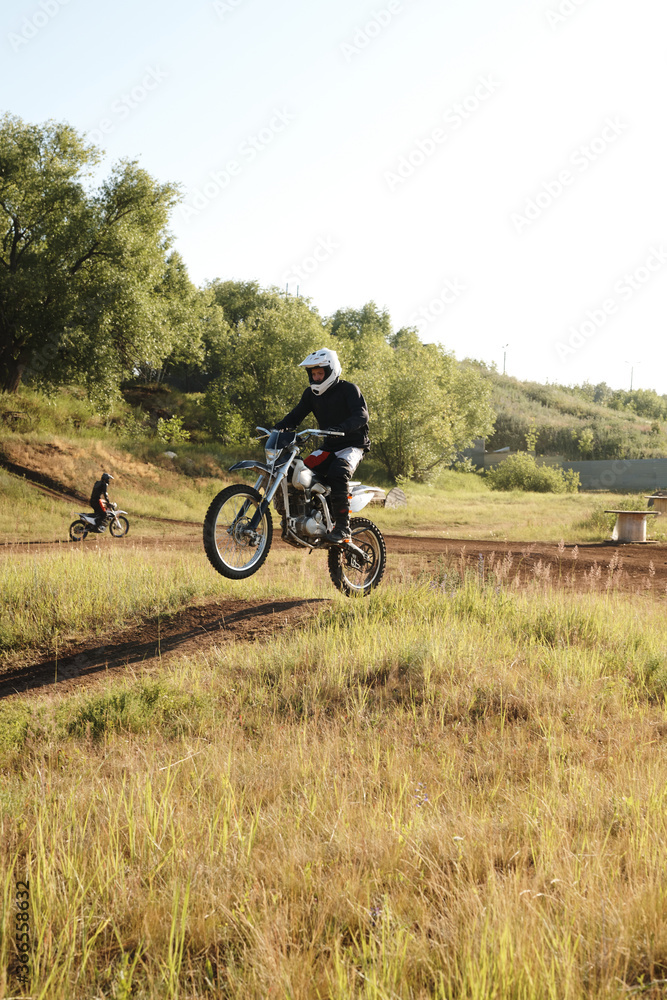 Professional motorcyclist in helmet making step-up while riding motorbike on rough track Professional motorcyclist in helmet making step-up while riding motorbike on rough track