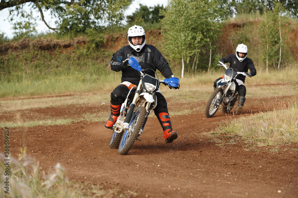 Obraz premium Men in protective outfits enjoying motorcycling on dirty road while competing against each other on rough track