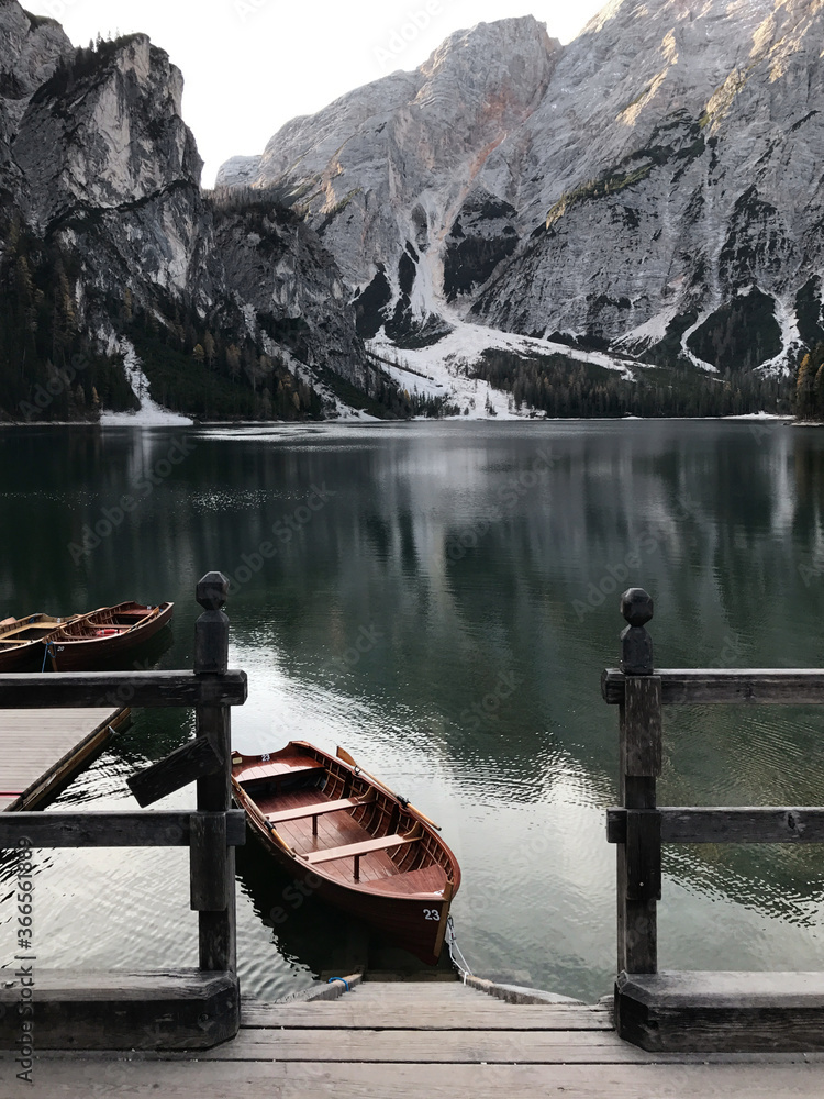An old wooden boat stands near a boat station on a lake with a reflection of the mountains
