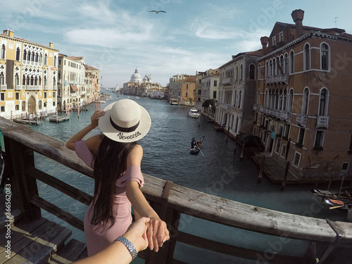 Follow me. View on Grand canal with woman traveler in hat on Academia bridge in Venice.