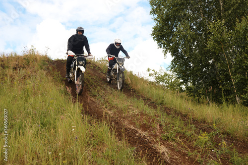 Active motorcyclists in helmets riding motorbike downhill while developing their skill at off-road track