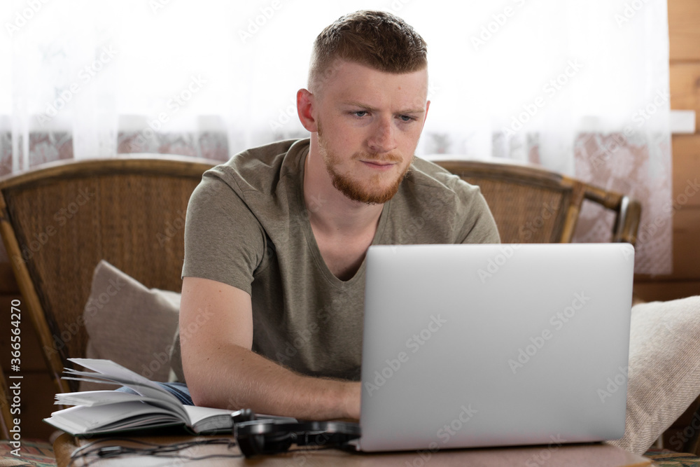 Portrait of a caucasian employee working remotely from home using laptop. Work in the living room. Man typing on computer. Man sitting at wooden table and working. Portrait of a caucasian employee working remotely from home using laptop. Work in the living room. Man typing on computer. Man sitting at wooden table and working.