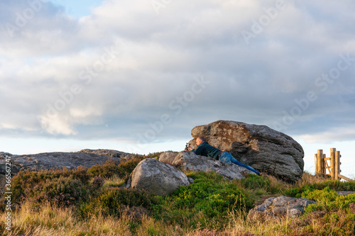 Man laying on stone and taking photos of the landscape on phone against cloudy sky © Iryna