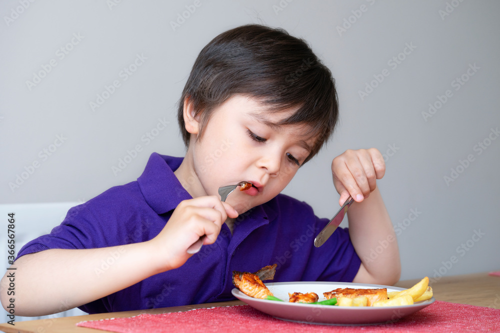 Healhty kid eating homemade salmon steak and chips for his sunnday dinner at home, Portrait of Child boy learning how to use knife and fork by him self, Healthy food for Children concept Healhty kid eating homemade salmon steak and chips for his sunnday dinner at home, Portrait of Child boy learning how to use knife and fork by him self, Healthy food for Children concept