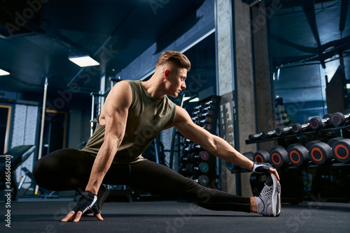 Bodybuilder stretching on floor in gym.