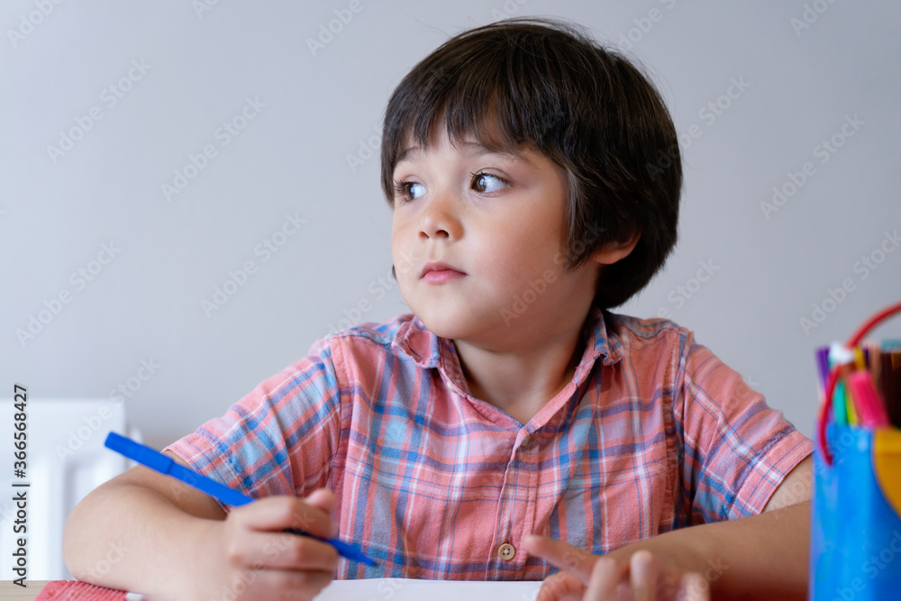 Portrait of school kid boy siting on table and looking out with thinking face, Child holding blue paint colour, Elementary school and education concept Portrait of school kid boy siting on table and looking out with thinking face, Child holding blue paint colour, Elementary school and education concept