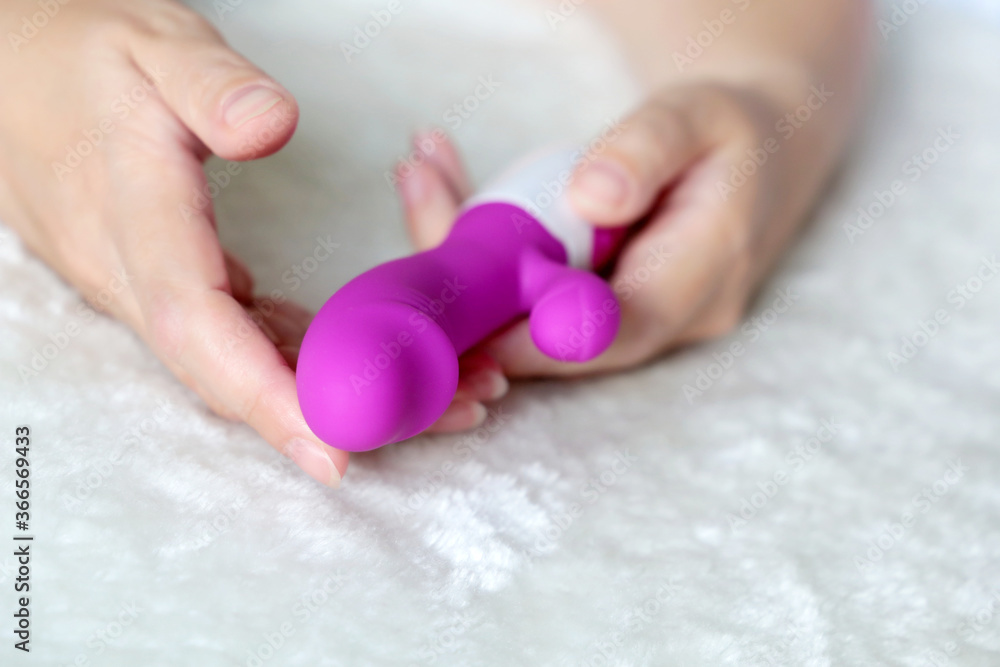 Dildo in female hands close up. Woman on a bed with purple silicone vibrator for sex games Dildo in female hands close up. Woman on a bed with purple silicone vibrator for sex games