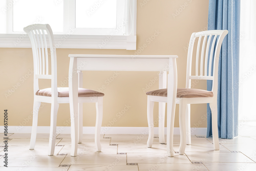 Fototapeta premium Two white chairs and white empty table by the window in a clean large room