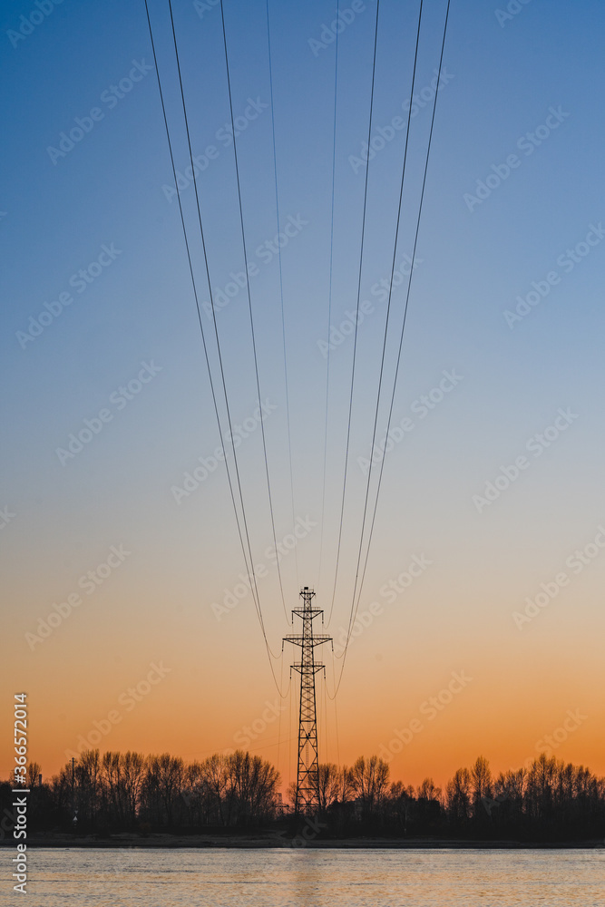 High voltage power lines at sunset. Beautiful landscape. Lonely silhouette against the background of the beautiful sky and the river.