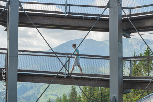 Fotografia Young adult caucasian man walking up on an elevated walkway with nature and moun