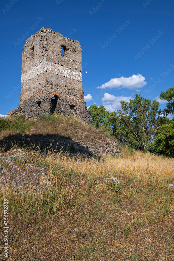 Front view of the imposing Selce Tower made of stone, along the Via Appia Antica or Appian way. Summer day with vast meadow clouds, yellowed grass from the sun. Deep blue sky. Rome Italy.