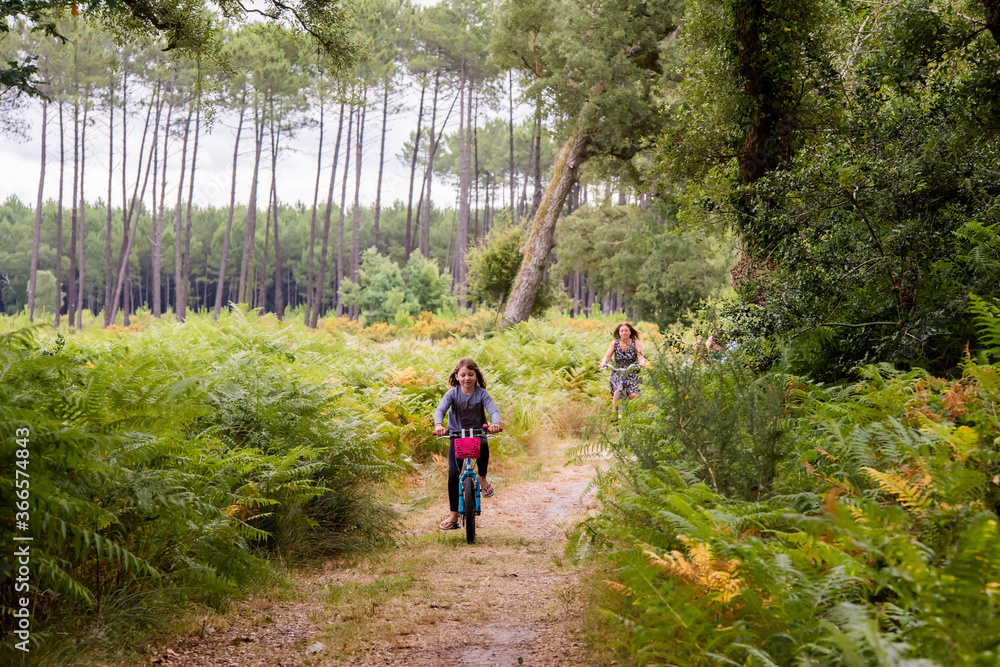 Fototapeta premium cute little girl riding a bicycle in the forest with her mom