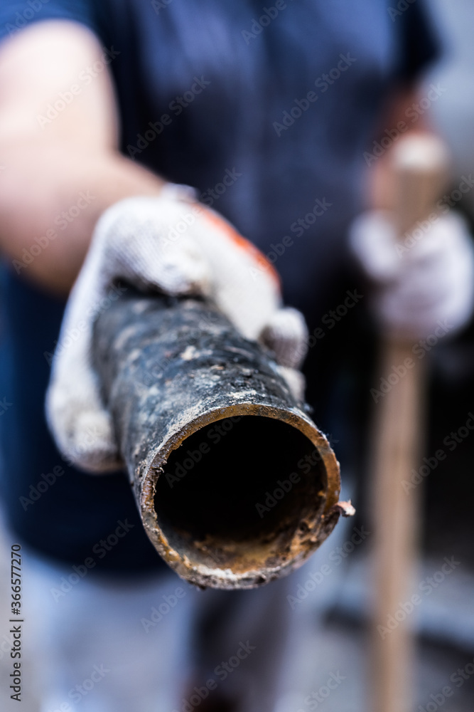 A worker holds in his hands piece of a metal pipe cut off