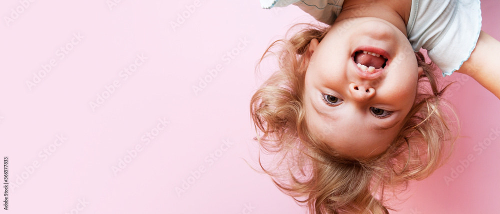 cute funny baby upside down looking at camera on pink background with copy space