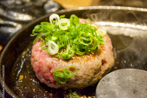 熱々の鉄板の上で湯気の立ち上る、まだ半生の調理中の手ごねハンバーグ、たっぷりの刻みネギ。一人前。外食、昼ご飯、食堂、オープンキッチン。口コミ、グルメ、行列、人気店。レストランあさくま考案のペレット。