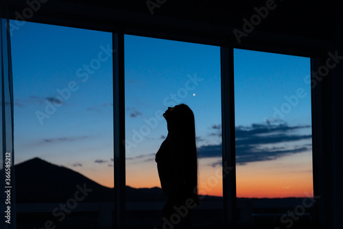 Silhouette of a girl against sunset on the window mountains view © Vasya