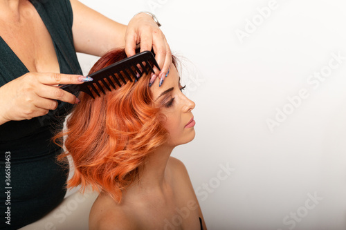 Beautiful redhead woman getting her hair comb by professional female hairdresser.