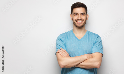 Banner of young handsome man wearing blue t-shirt, standing with crossed arms, isolated on studio gray background
