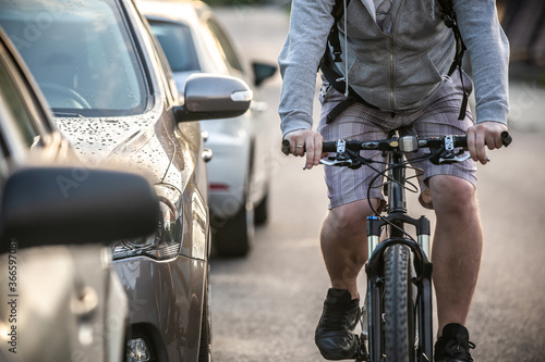 An unidentified man riding a bicycle passing cars on the road.