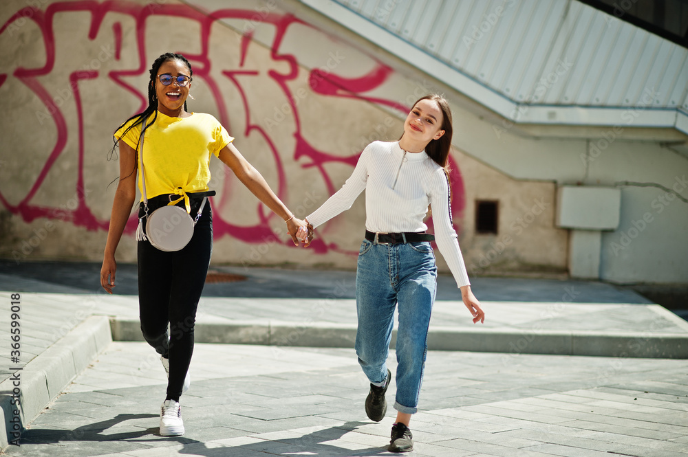 Obraz premium White caucasian girl and black African American together against graffiti wall. World unity, racial love, understanding in tolerance and races diversity cooperation.