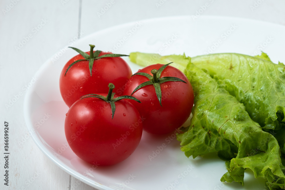 cherry tomatoes with a leaf of lettuce on a white plate