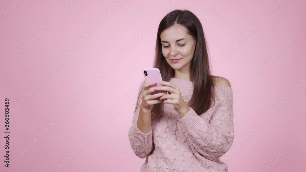 Portrait of woman in pink sweater uses mobile phone, isolated on pink background Portrait of woman in pink sweater uses mobile phone, isolated on pink background