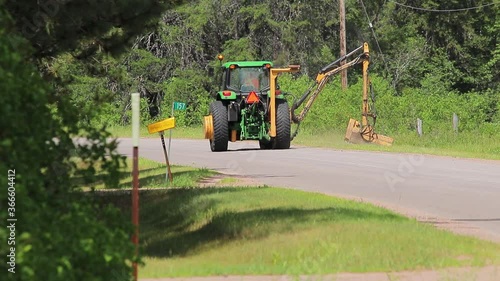 Killaloe, Ontario, Canada / July, 23, 2020 :  John Deere tractor cutting brush in ditch of road.  drives around corner out of sight
