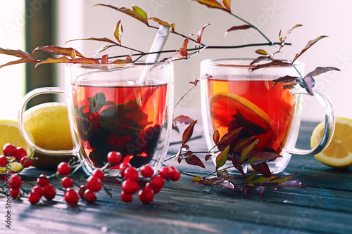 Two transparent glass cups of hot berry tea with lemons  in autumn leaves decoration, winter autumn mood, citrus red tea, autumn concept, close up