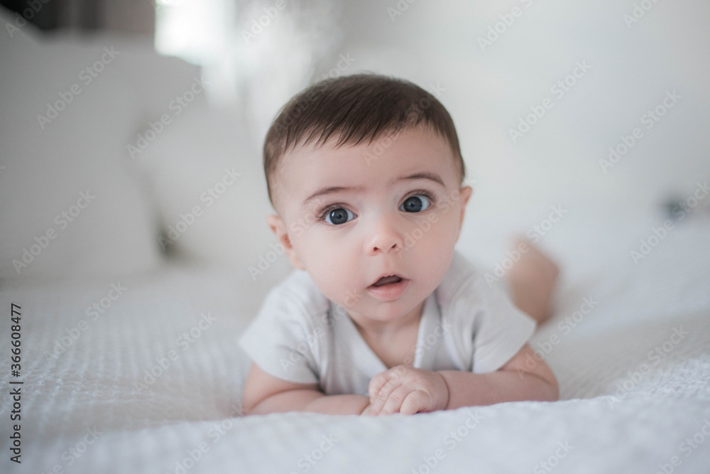 Baby in white bed bed playing looking at he camera serious face tummy time Baby in white bed bed playing looking at he camera serious face tummy time