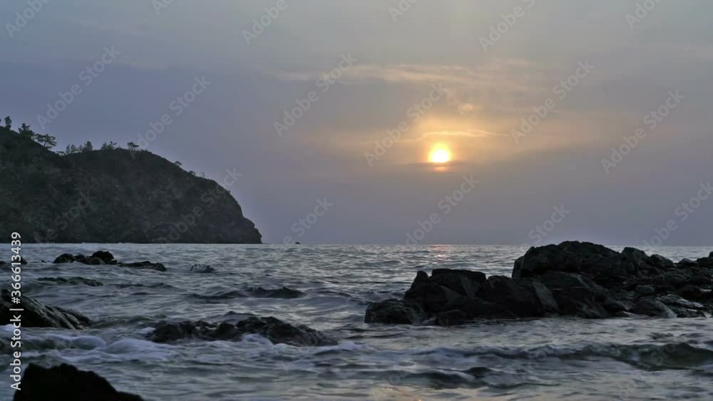 Sunrise over the sea. The sun rises from behind the clouds. The waves wash the silhouette of stones. Sunrise over the sea. The sun rises from behind the clouds. The waves wash the silhouette of stones.