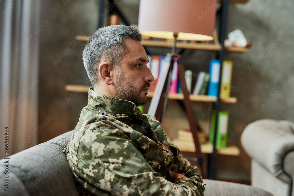 Middle aged military man looking away, sitting on the couch during therapy session. Soldier suffering from depression, psychological trauma. PTSD concept Middle aged military man looking away, sitting on the couch during therapy session. Soldier suffering from depression, psychological trauma. PTSD concept