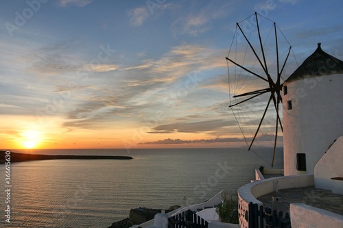 windmill in sunset at Oia  Santorini  orange sun light  blue sky  white clouds