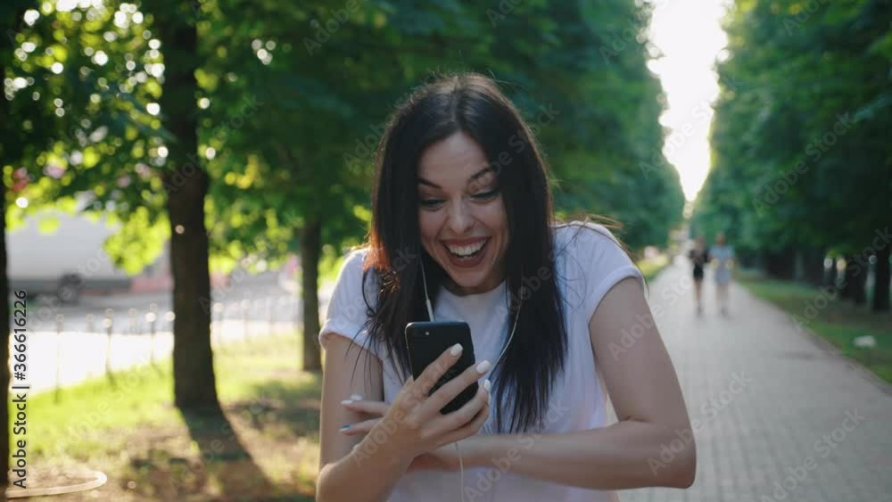 Portrait of happy young woman enjoy success on mobile phone while walking city. Excited joyful girl reading good news on phone in slow motion. Surprised lady celebrating victory outdoors on sunset. Portrait of happy young woman enjoy success on mobile phone while walking city. Excited joyful girl reading good news on phone in slow motion. Surprised lady celebrating victory outdoors on sunset.
