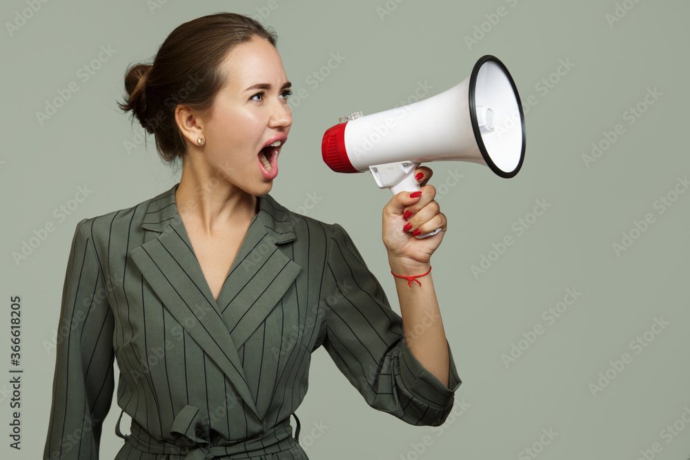 A woman shouts into a megaphone. Business suit on a green background A woman shouts into a megaphone. Business suit on a green background
