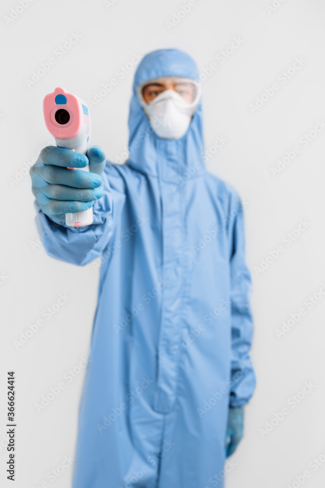 male doctor in a protective suit from the coronavirus, a medical mask glasses and gloves, uses an infrared non-contact thermometer gun to check body temperature for symptoms of the covid-19 virus male doctor in a protective suit from the coronavirus, a medical mask glasses and gloves, uses an infrared non-contact thermometer gun to check body temperature for symptoms of the covid-19 virus