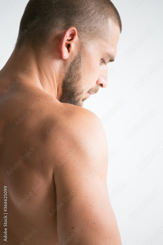 young man with neck pain. A man with a naked athletic torso poses in a photo studio on a white background. A healthy image of a strong, well-trained male body. Shows the muscles.